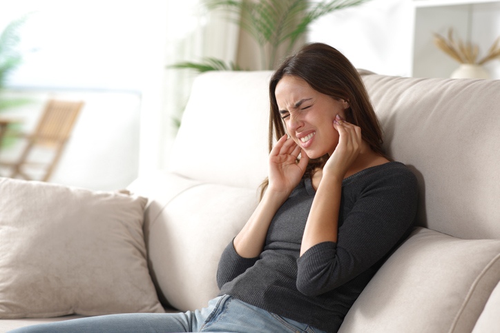 Person holding jaw with TMJ pain while sitting on couch in South Bend, IN